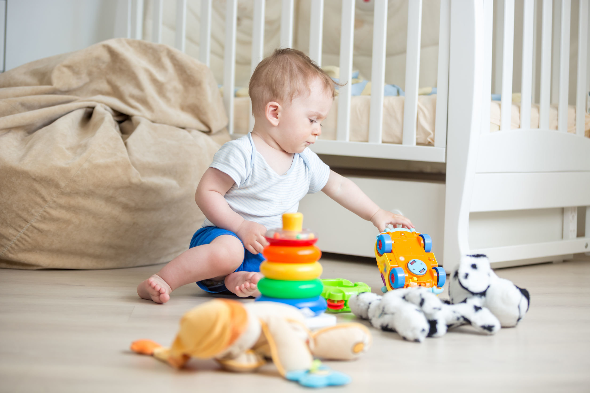 Kleines Kind sitzt auf dem Boden und spielt mit Stofftieren und anderem Spielzeug in seinem Zimmer